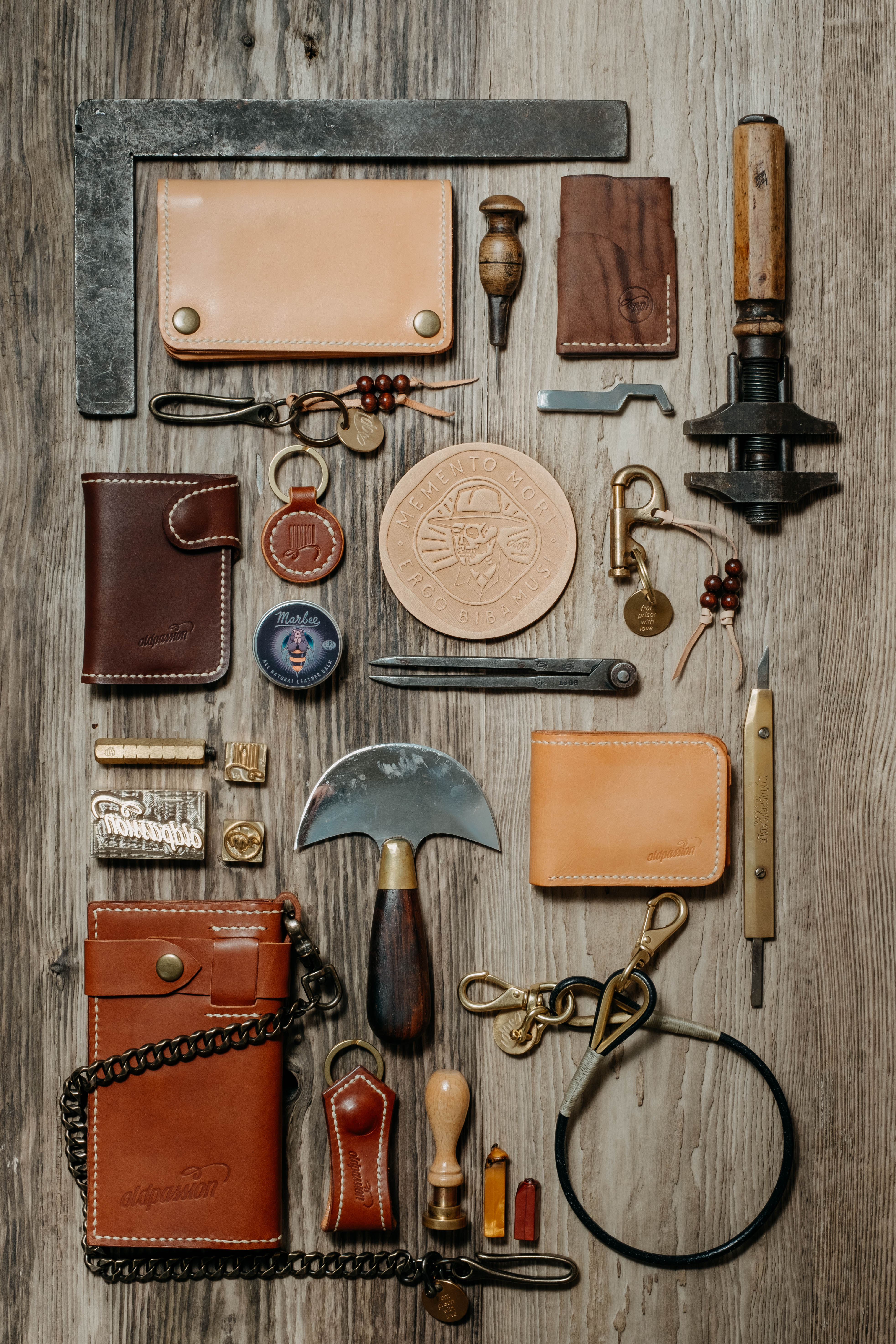 oldpassion Lederwaren im Flatlay: Portemonnaies, Schlüsselanhänger und Lederwerkzeug auf Holz